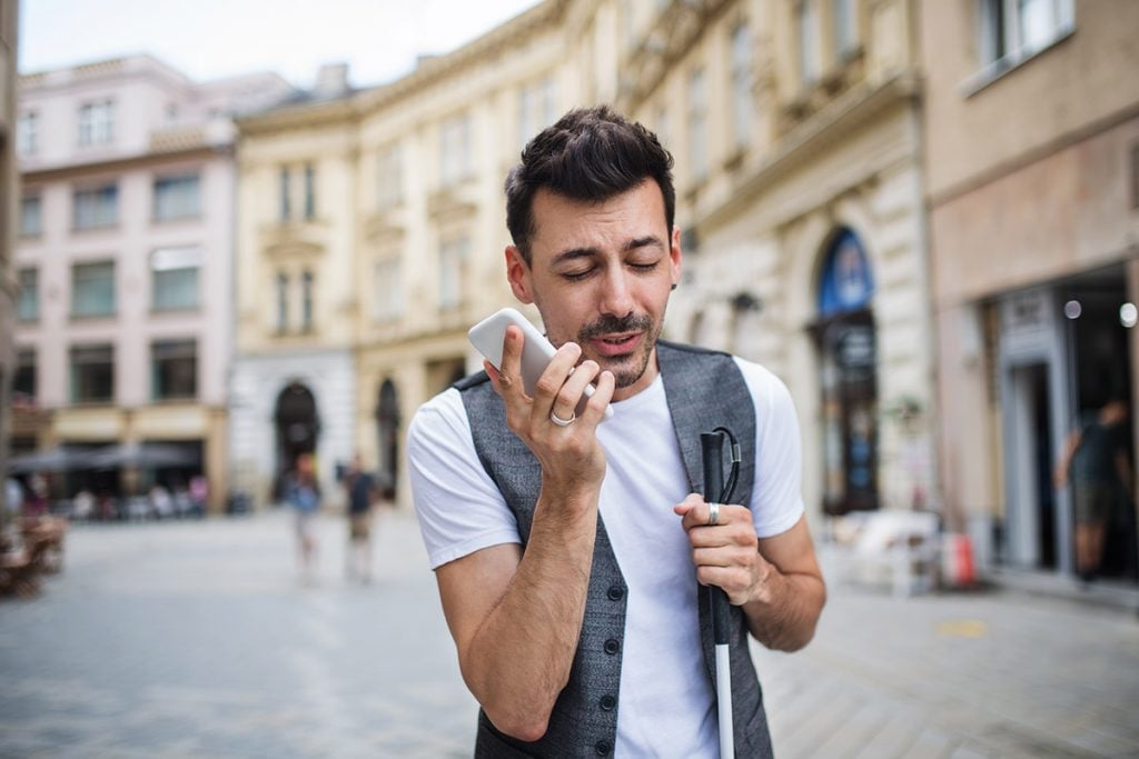 Young blind man with smartphonee on street in city