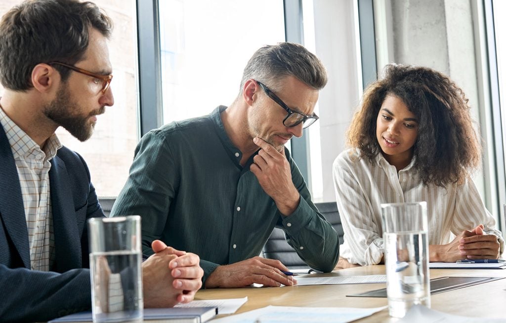 2 male investment managers and a female investment manager inspecting a financial document