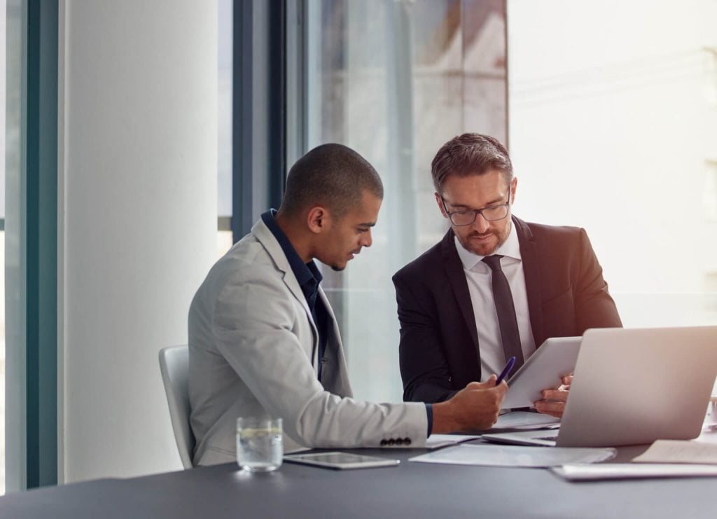 Two investment management professionals reviewing regulatory reporting documents at a laptop