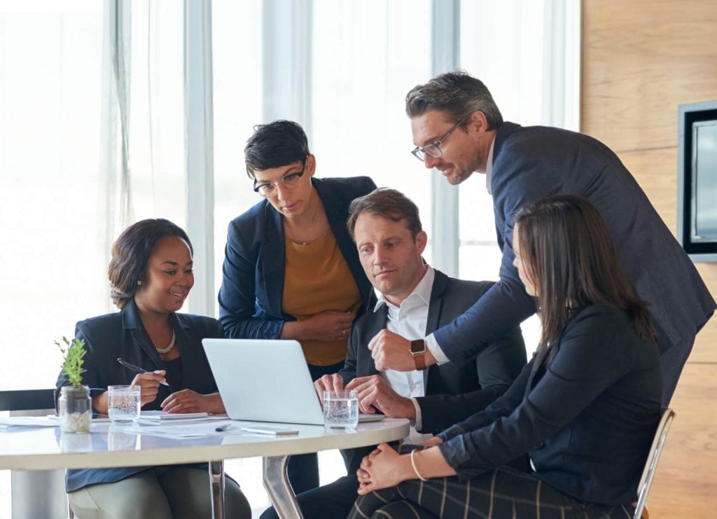Compliance and investment management professionals collaborating around a laptop to review CCI regulatory reporting