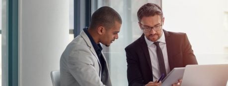 Two investment management professionals reviewing regulatory reporting documents at a laptop